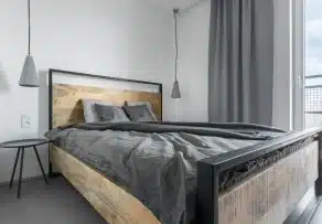 Modern wooden bed frame with a black metal frame and grey bedding in a minimalist bedroom in Malaysia