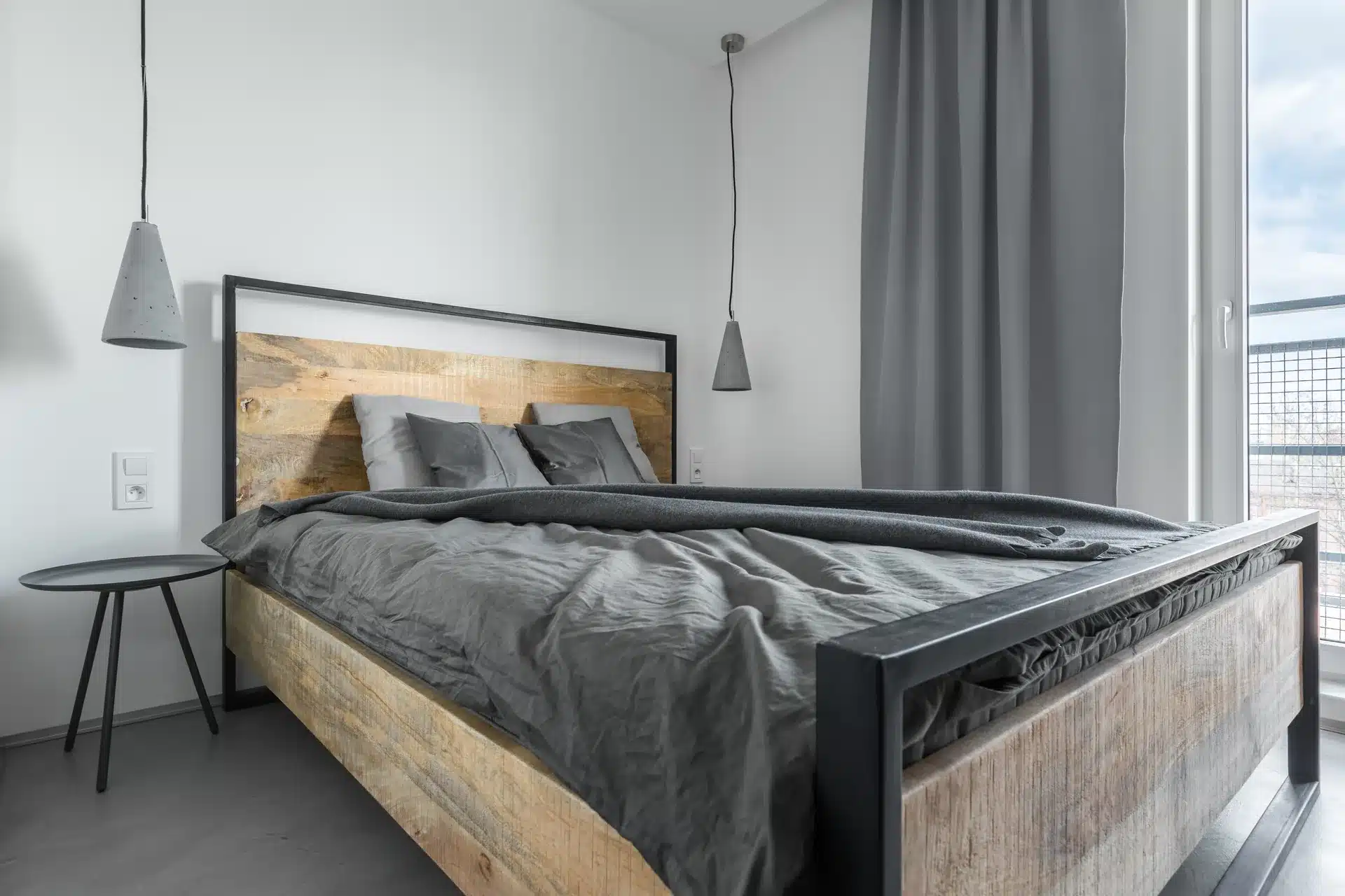 Modern wooden bed frame with a black metal frame and grey bedding in a minimalist bedroom in Malaysia