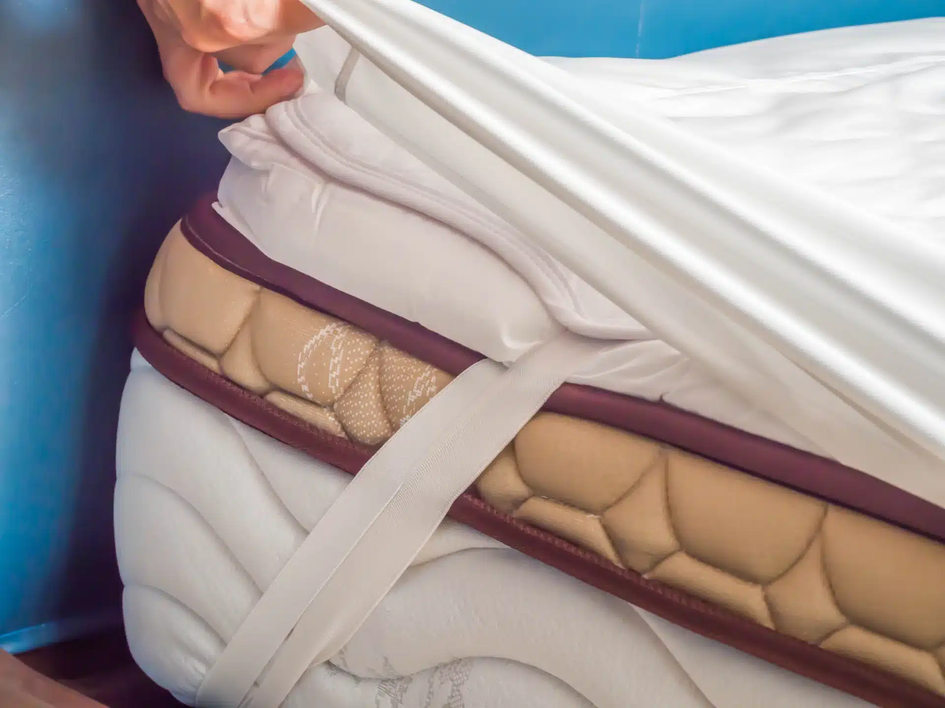 A person fitting a white, waterproof mattress protector malaysia over a bed corner to guard against sweat and moisture.